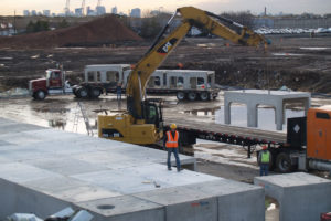 An Excavator unloading large prefab concrete structures off of a flatbed truck.