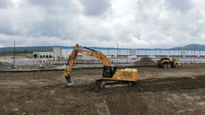 A tracked excavator spreading topsoil in front of a warehouse.